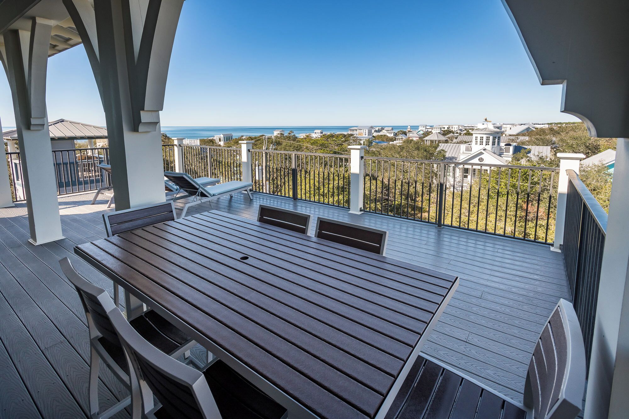 Une terrasse en bois avec une table et des chaises, donnant sur une zone côtière avec des bâtiments et de la végétation.
