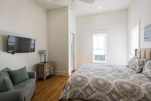 Ein Schlafzimmer mit einem Bett, einem Fernseher, einem Nachttisch, einer Lampe, einem Sofa und einem Fenster.