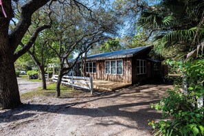 A rustic cabin with a wooden deck, surrounded by trees and greenery. - Walk to Beach & Grayton Beach- Artless Sprite by Royal Destinations (Santa Rosa Beach)