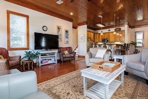 Ein Wohnzimmer mit Fernseher, zwei Sofas, einem Couchtisch und einer Küche im Hintergrund.