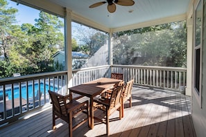 A covered outdoor deck with a table and chairs, a ceiling fan, and a view of a swimming pool and trees. - Private Pool, Steps From Seaside- Billiken Bungalow by Royal Destinations (Santa Rosa Beach)