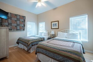 Ein Schlafzimmer mit zwei Betten, einem Deckenventilator und einem an der Wand befestigten Fernseher.