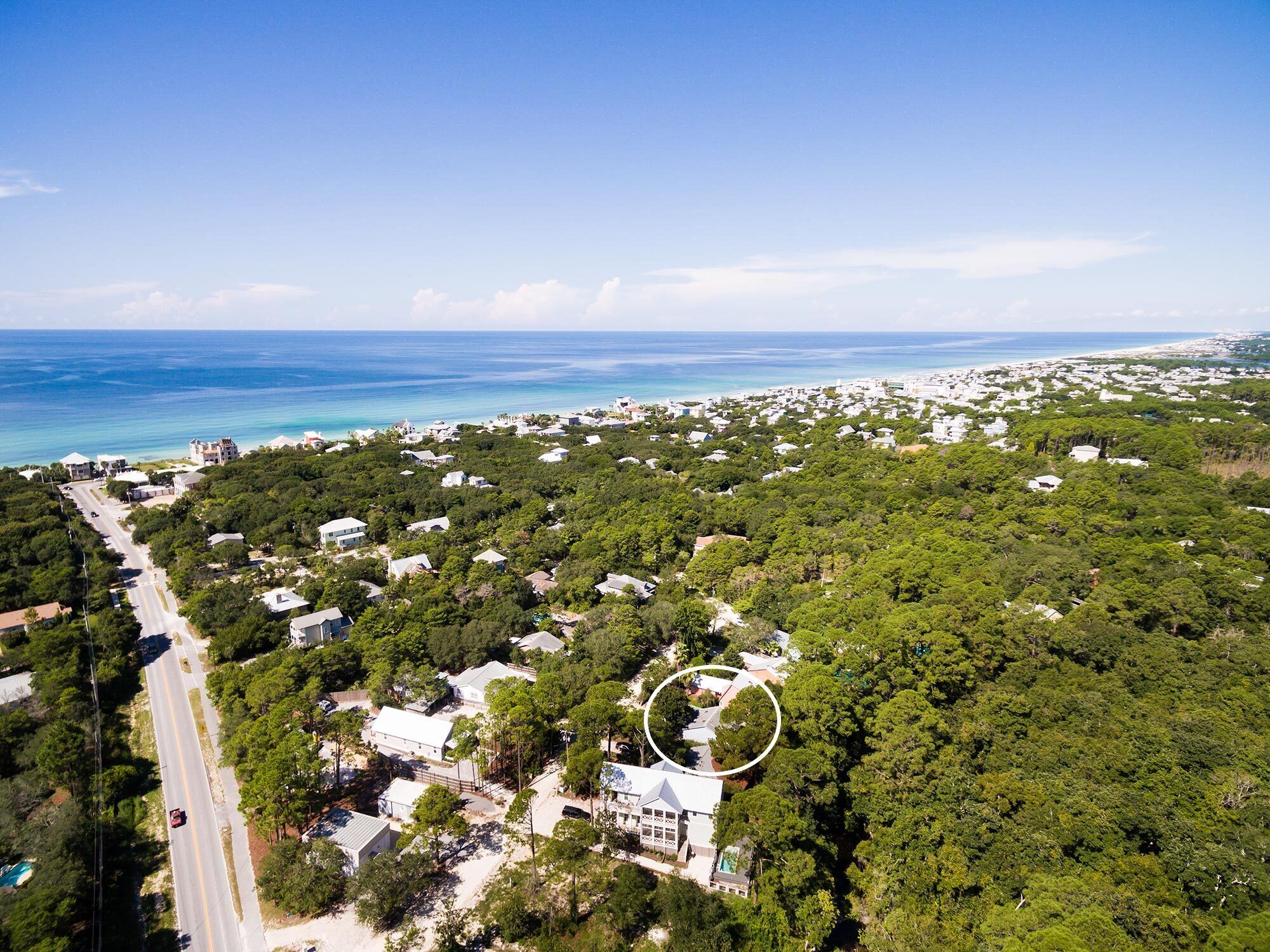 Vista aerea di una zona costiera con vegetazione rigogliosa, una strada e una spiaggia sullo sfondo.