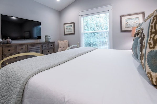 A bedroom with a bed, a TV, a dresser, and a window with blinds.