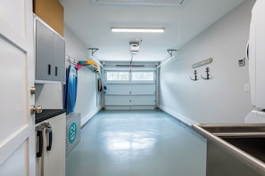 A clean, well-lit corridor with a kitchenette area on the right, a door with a 'Beach House' sign, and a row of kayaks on the left.