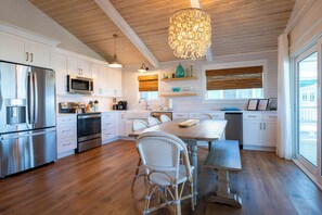 A modern kitchen with white cabinetry, stainless steel appliances, wicker chairs, and a large dining table. - Gulf & State Park Views, Near Beach Access- Dune Watch by Royal Destinations (Santa Rosa Beach)