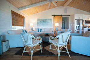 A spacious living room with two sofas, a coffee table, wicker chairs, and a kitchen area with modern appliances. - Gulf & State Park Views, Near Beach Access- Dune Watch by Royal Destinations (Santa Rosa Beach)