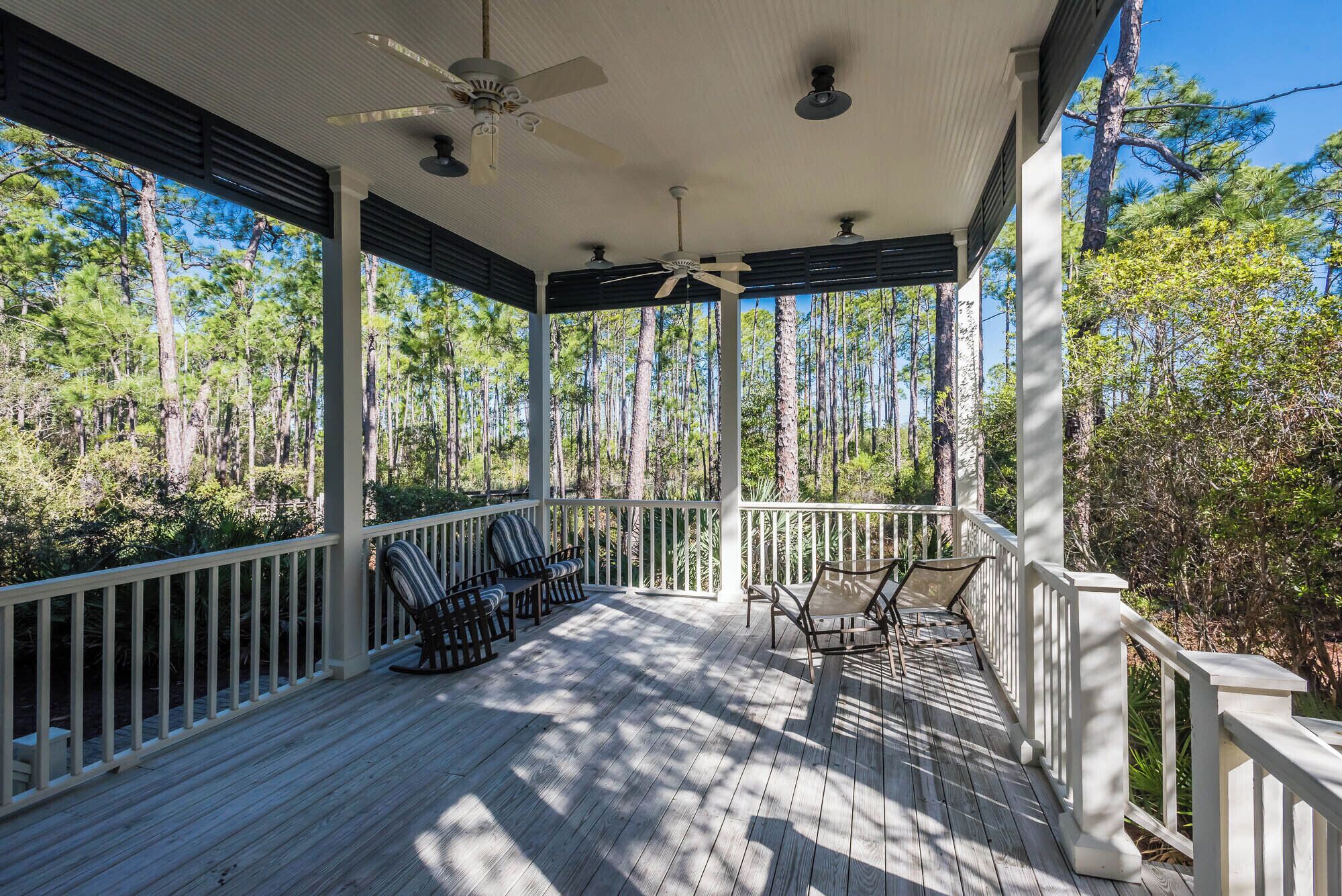 A covered wooden deck with white railings, ceiling fans, and chairs.