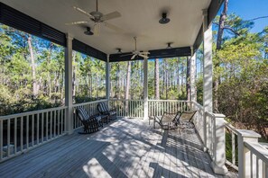 Eine überdachte Holzterrasse mit weißen Geländern, Deckenventilatoren und Stühlen.