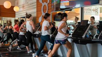 Un grupo de personas ejercitándose en cintas de correr en un gimnasio, con un marcador digital y citas motivacionales en la pared.