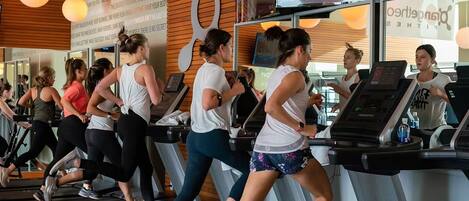 A group of people exercising on treadmills in a gym with a digital scoreboard and motivational quotes on the wall.