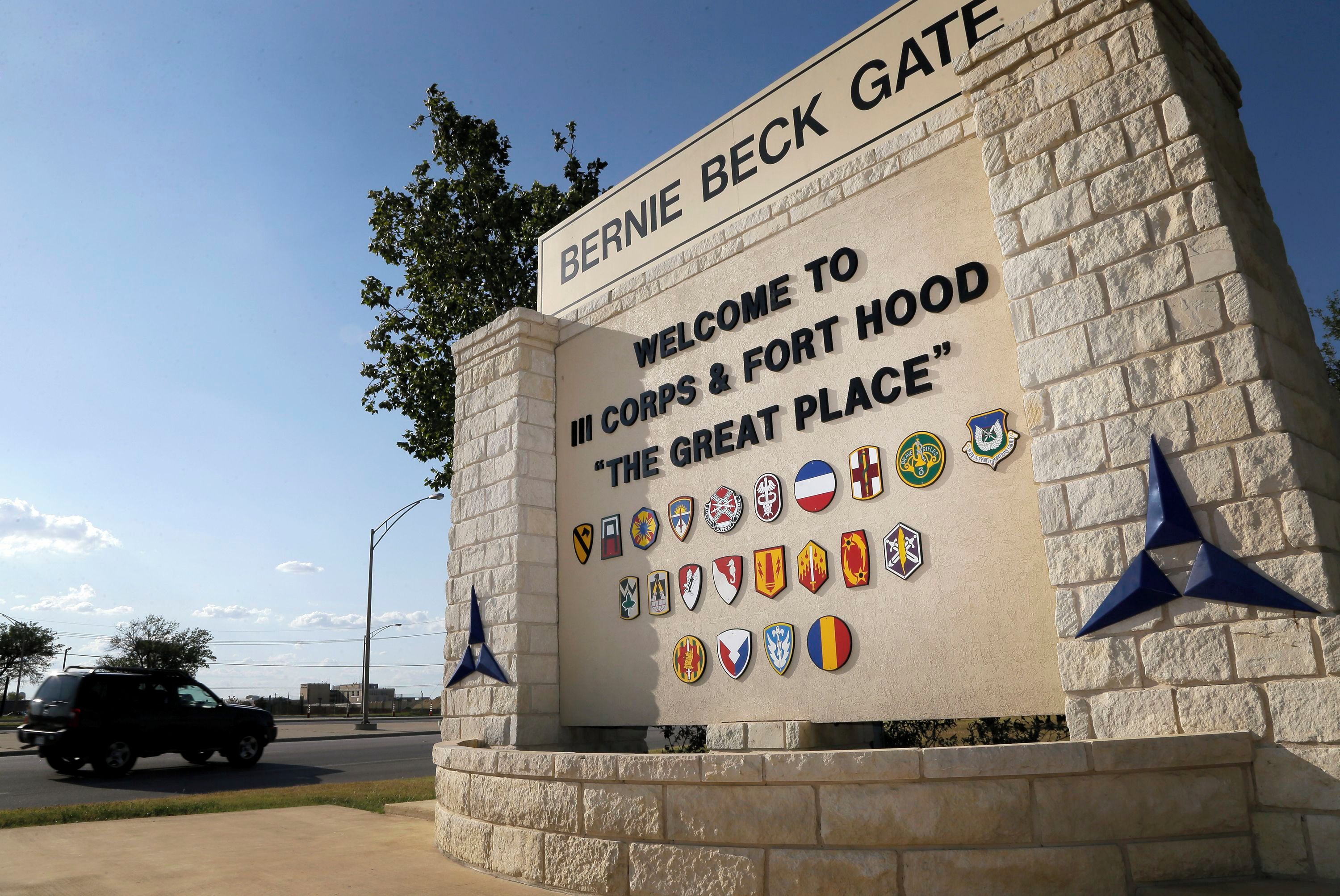 A sign with 'BERNIE BECK GATE' and 'WELCOME TO IF CORPS & FORT HOOD' with various military unit badges.