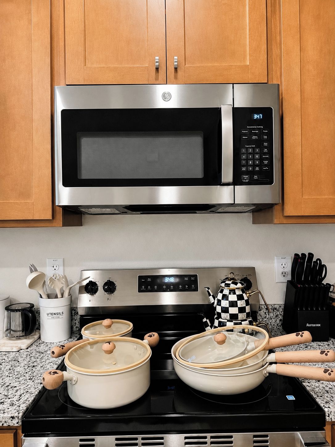 A kitchen with a stainless steel microwave, a stove, and pots on the counter.