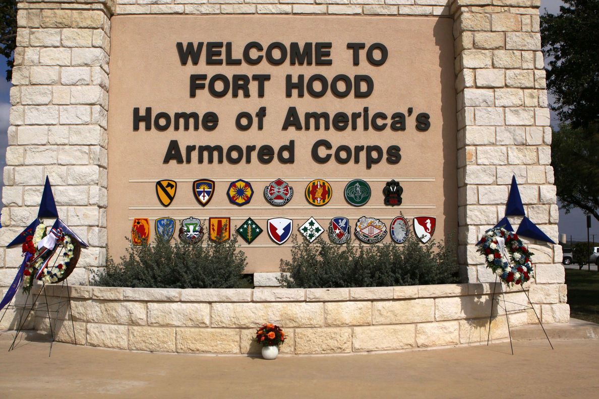 A welcome sign for Fort Hood, home of America's Armored Corps, with military unit emblems and flags.