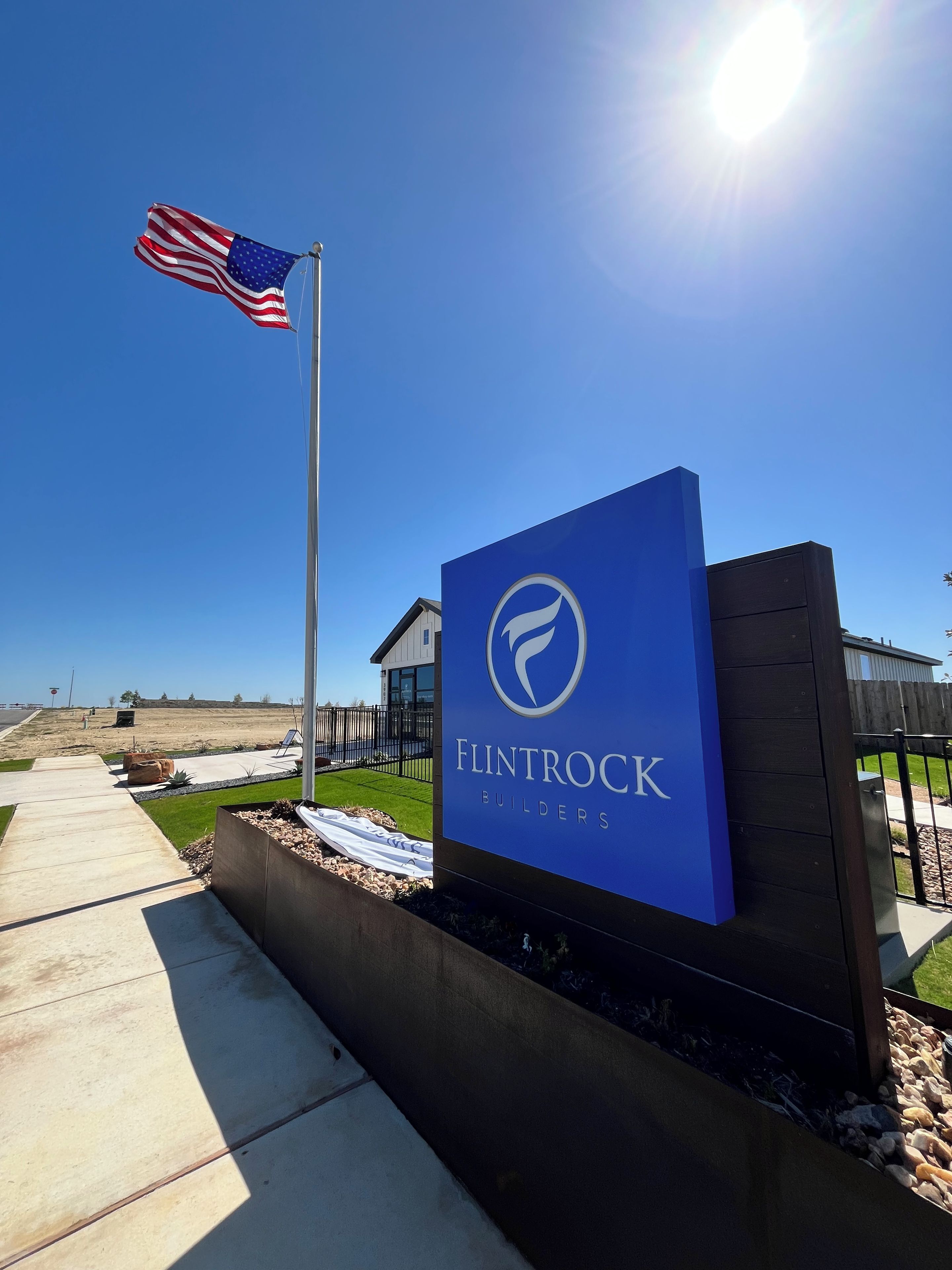 A sign for Flintrock Builders with a clear sky and a flag in the background.