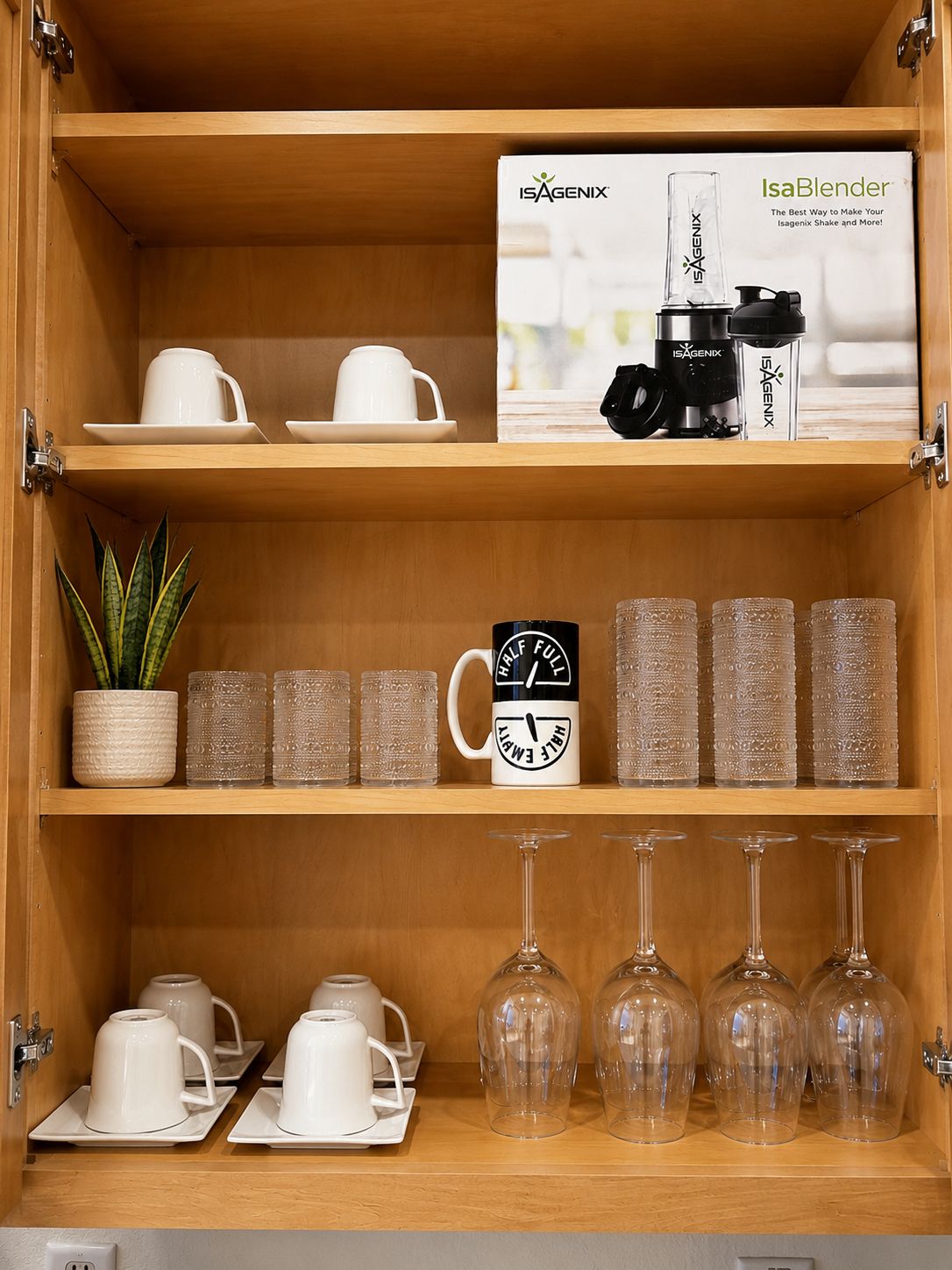A wooden cabinet with shelves containing various items including a box labeled 'Isagenix', a mug, glassware, and a potted plant.