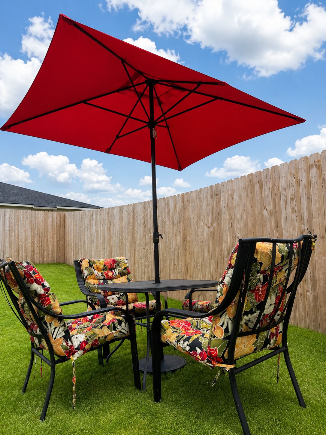 A patio with a red umbrella, two chairs with floral upholstery, and a wooden fence in the background.