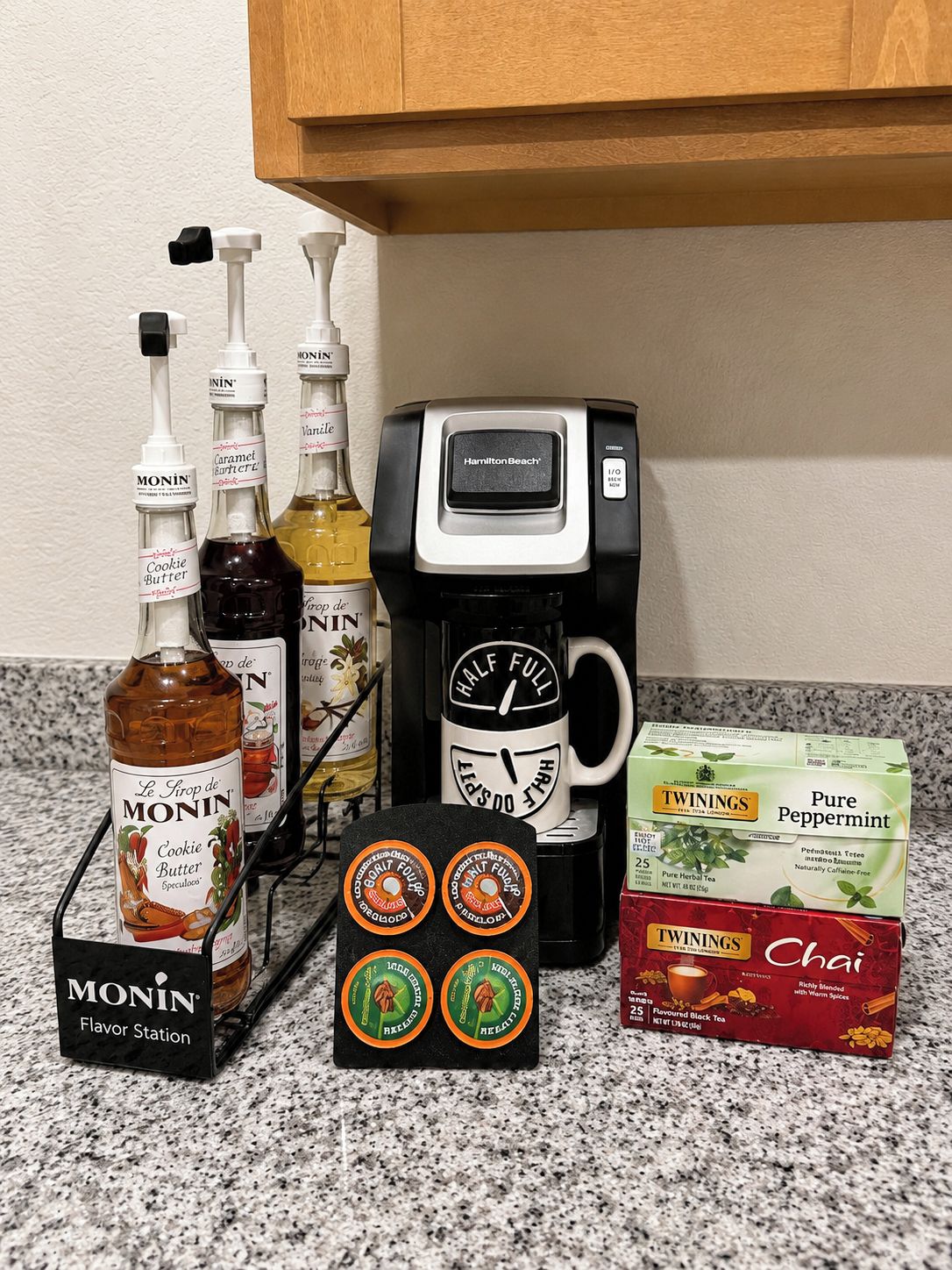 Een aanrecht met diverse spullen, waaronder een koffiezetapparaat, flesjes kruiden, een mok en theedoosjes.