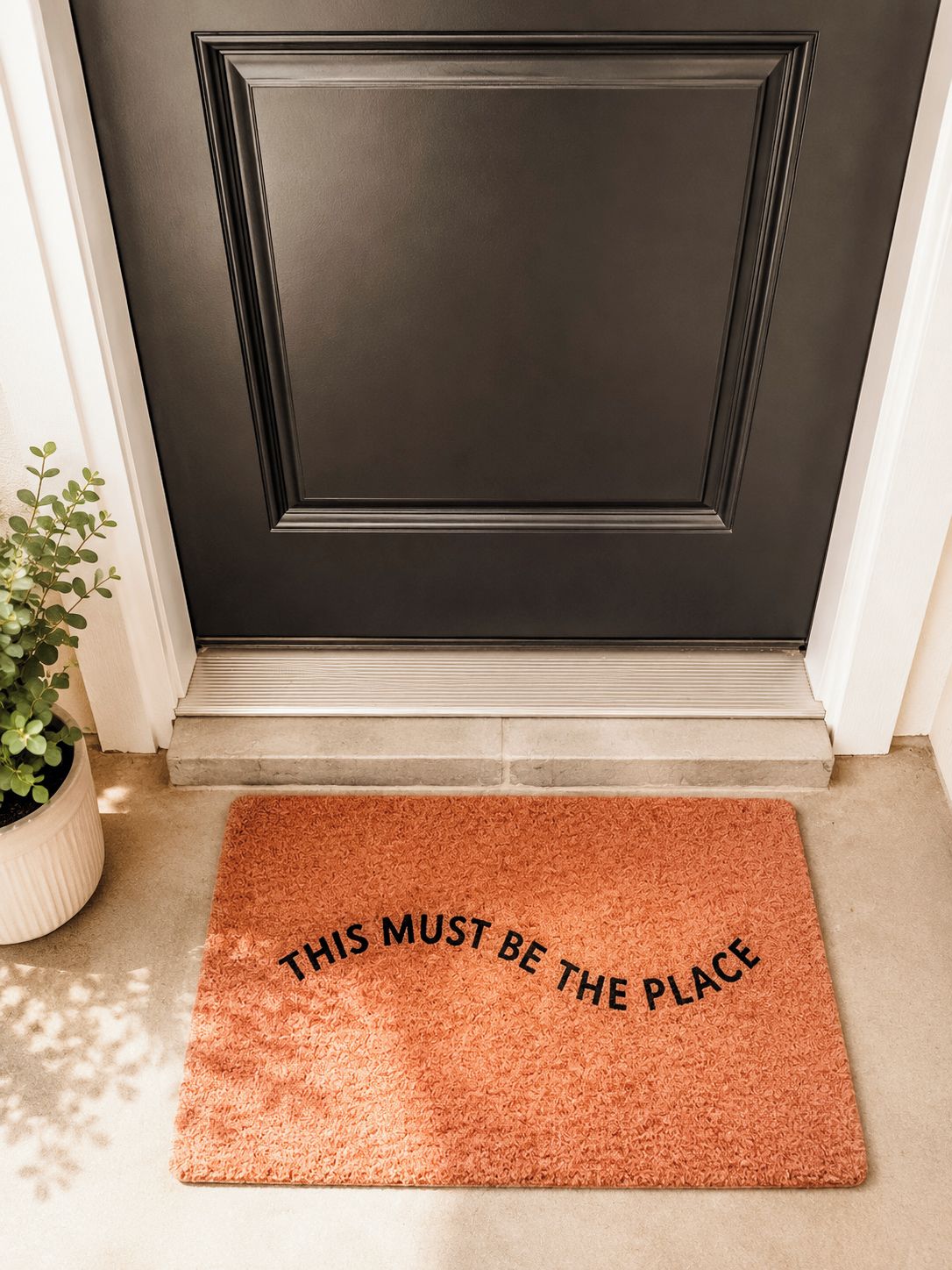 Una porta scura con un tappetino sagomato con la scritta 'THIS MUST BE THE PLACE'.