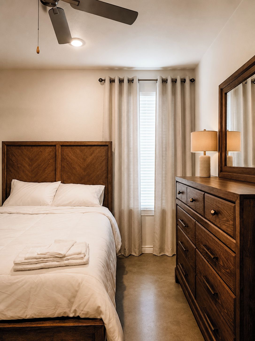 Une chambre d’hôtel avec un lit, une commode, un ventilateur de plafond et une fenêtre avec des rideaux.