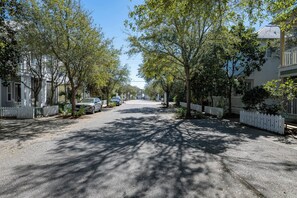 A residential street lined with trees and houses, with parked cars and a clear sky.