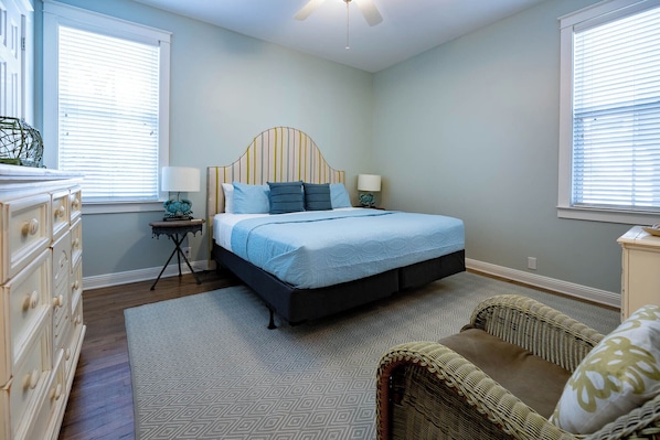 Une chambre à coucher comprenant un lit, une commode, une table de chevet, une lampe et un ventilateur de plafond.