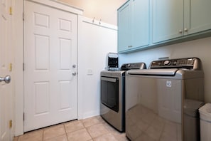A laundry room with a white door, a washing machine, a dryer, and a trash bin.