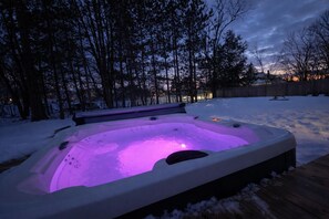 Lämmin poreallas lumisen takapihan keskellä, puinen terassi ja puita taustalla.