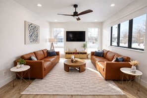 A modern living room with two leather sofas, a coffee table, and a ceiling fan. - Biji Blue! Private Hot Tub, 2 Ensuite Bedrooms! (Bemidji)
