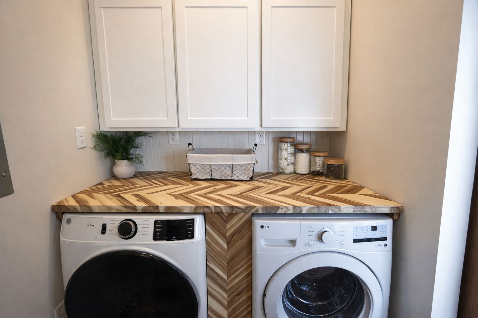 A laundry room with two washing machines, a wooden countertop, cabinets, and a potted plant.