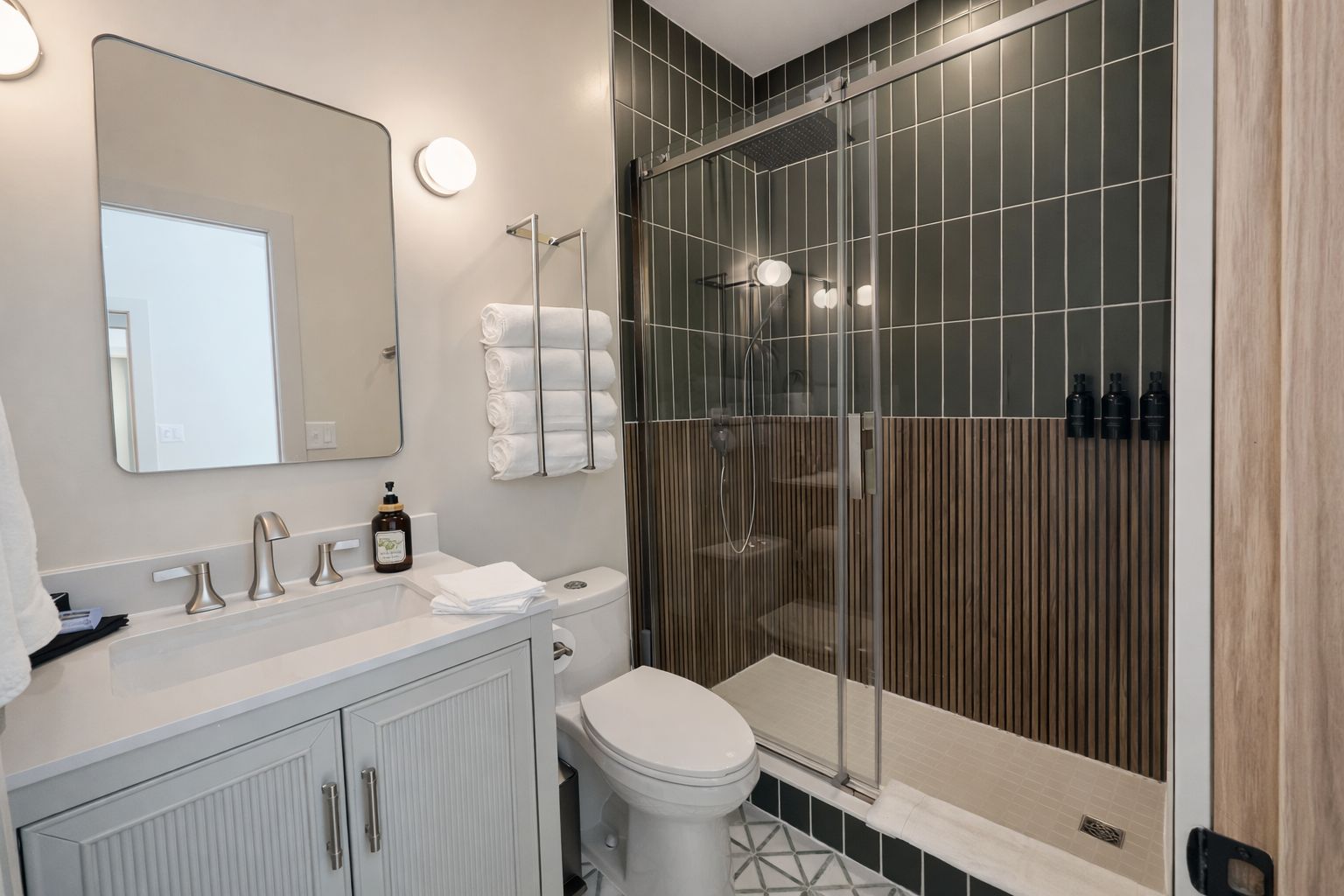 Een moderne badkamer met een grote spiegel, een toilet, een wastafel met zeepdispenser en een douchecabine.
