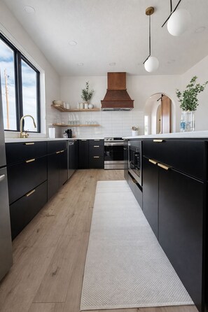 A modern kitchen with black cabinetry, a central island, and a wooden floor. - Biji Blue! Private Hot Tub, 2 Ensuite Bedrooms! (Bemidji)
