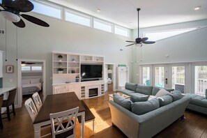 A spacious living room with a large grey sofa, a dining table with chairs, a TV, and ceiling fans. - Pet Friendly with Private Pool, Near Beach- Gindarra by Royal Destinations (Santa Rosa Beach)
