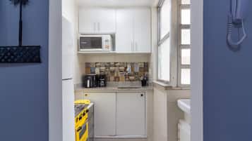 Cocina compacta con armarios blancos, microondas, cafetera y estufa a gas amarilla.