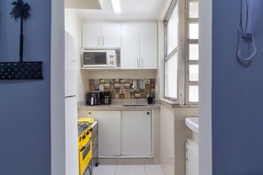 Eine kompakte Küche mit weißen Schränken, einer Mikrowelle, einer Kaffeemaschine und einem gelben Gasherd.