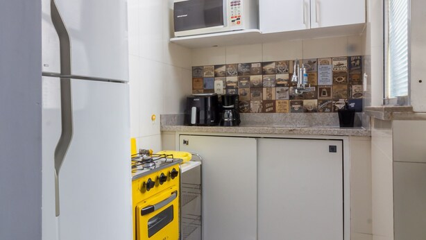 A compact kitchen with white cabinets, a microwave, a gas stove, and a yellow cart. - 7 Mins From Copacabana Beach Pfa603 (Rio de Janeiro)
