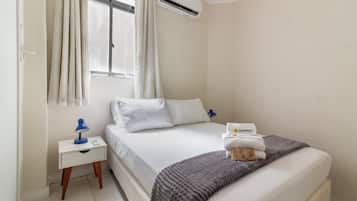 Habitación de hotel con cama, mesita de noche, lámpara, ventana con cortinas y aire acondicionado.