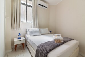 A hotel room with a bed, a nightstand, a lamp, a window with curtains, and an air conditioning unit. - 7 Mins From Copacabana Beach Pfa603 (Rio de Janeiro)
