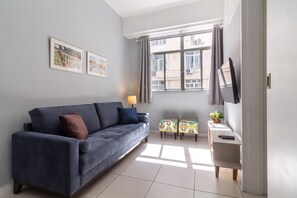 A living room with a sofa, a small table with a lamp, and a TV mounted on the wall. - 7 Mins From Copacabana Beach Pfa603 (Rio de Janeiro)