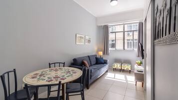 Una sala de estar con sofá, una mesa de comedor con sillas, televisor y ventana con cortinas.