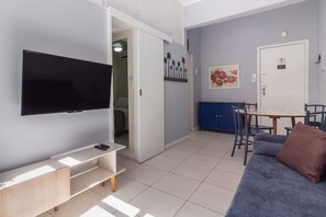Un saló modern amb un televisor de pantalla plana, un sofà, una taula de centre i una zona de menjador amb cadires.