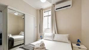 A hotel room with a bed, a nightstand, a mirror, an air conditioning unit, and a window with curtains. - 7 Mins From Copacabana Beach Pfa603 (Rio de Janeiro)