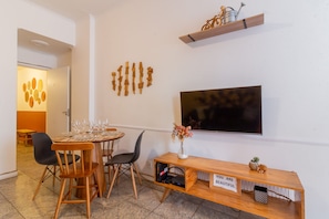 A dining area with a round table set for four, a television mounted on the wall, and a shelf above the table holding a bicycle and a watering can. - 2BR Apt Just 7 Mins to Copacabana Beach Br502 (Rio de Janeiro)