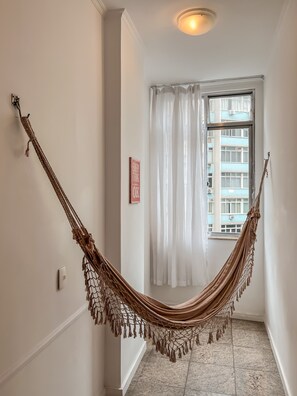 A hammock hanging from a wall in a hallway with a window and a door. - 2BR Apt Just 7 Mins to Copacabana Beach Br502 (Rio de Janeiro)