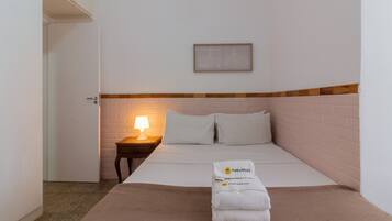 A hotel room with a bed, a nightstand with a lamp, a framed picture on the wall, and a towel with 'PINEAPPLES' on it.