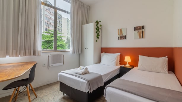 A hotel room with a bed, a desk, and a window with curtains. - 2BR Apt Just 7 Mins to Copacabana Beach Br502 (Rio de Janeiro)