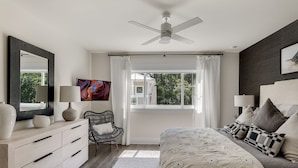 A bedroom with a bed, bedside lamps, a chair, a dresser, a ceiling fan, a window with curtains, and a painting on the wall. - Private Pool, Walk to Grayton Beach- Grayton Pointe by Royal Destinations (Santa Rosa Beach)