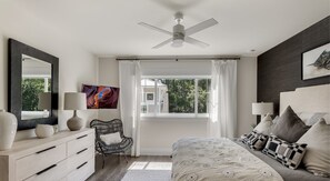 A bedroom with a bed, bedside lamps, a chair, a dresser, a ceiling fan, a window with curtains, and a painting on the wall. - Private Pool, Walk to Grayton Beach- Grayton Pointe by Royal Destinations (Santa Rosa Beach)