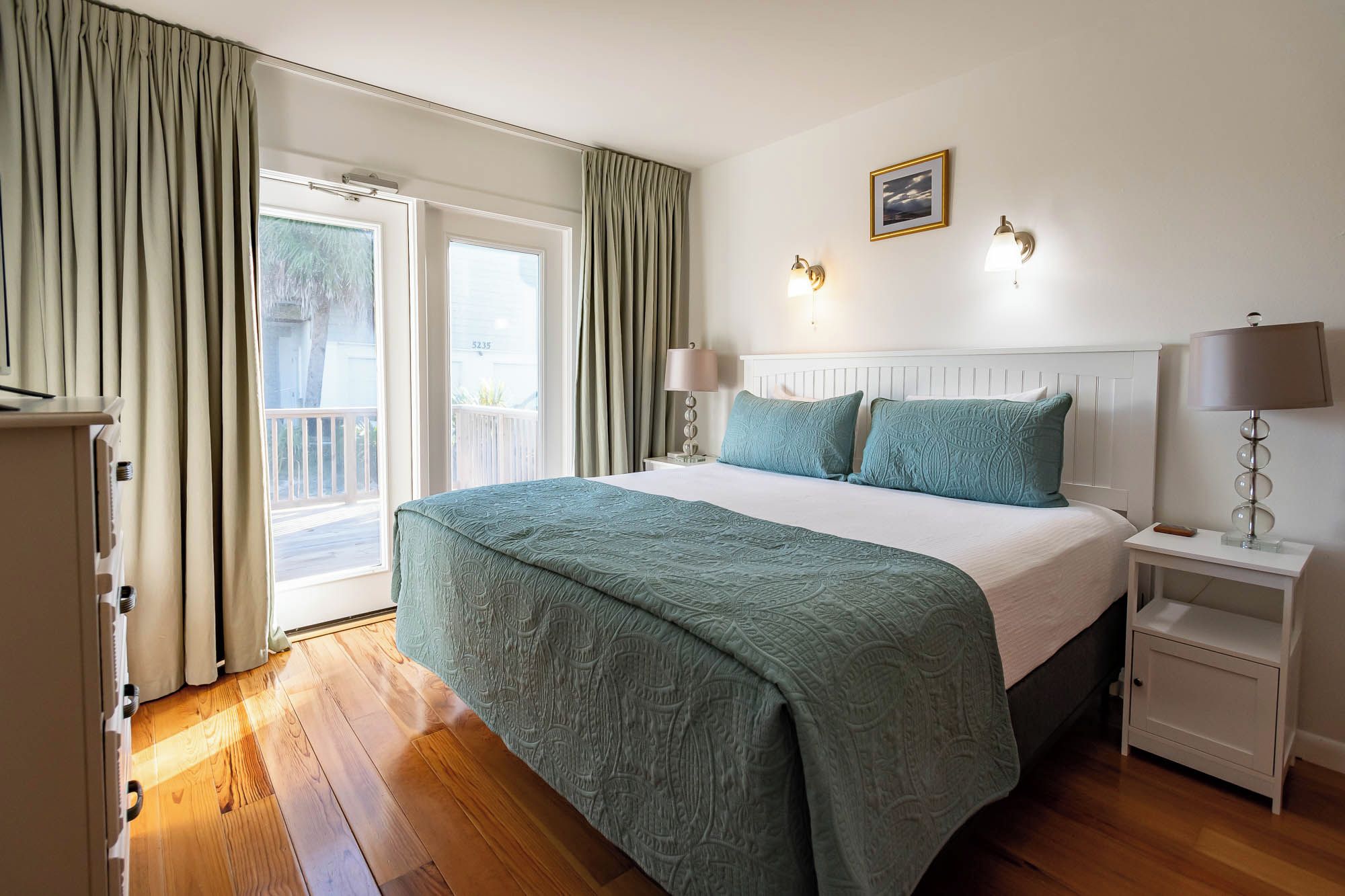 A hotel room with a large bed, two bedside lamps, a nightstand, a window with curtains, and a wall-mounted picture.