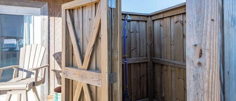 Une structure extérieure en bois, dotée d’une porte, d’une chaise et d’un tuyau d’arrosage.